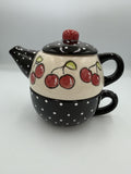 Ceramic tea for one set with red cherries on cream teapot stacked on black polka dot cup
