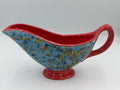 Blue speckled ceramic gravy boat with red rim, handle, and foot