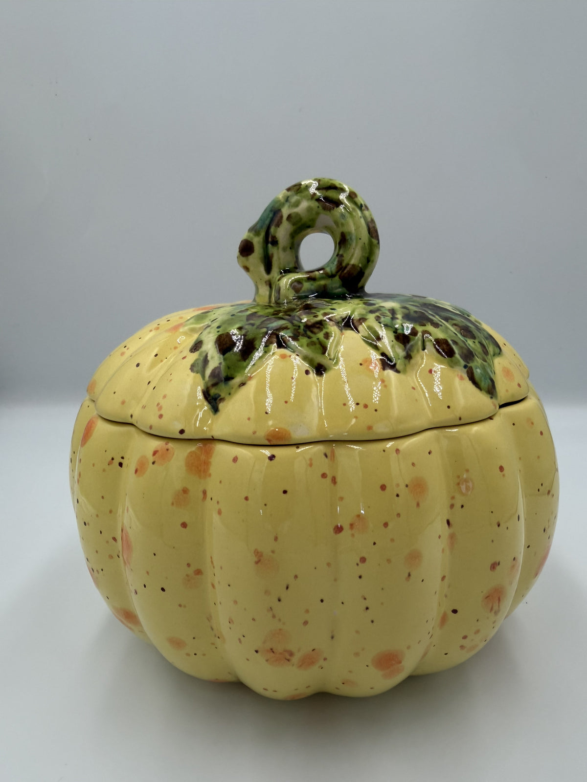 Yellow speckled ceramic harvest pumpkin with green leafy lid and curly stem