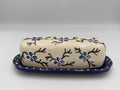 Cream ceramic butter dish lid painted with blue flowers and black branches on a cobalt tray with yellow dots