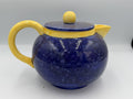 Large cobalt blue speckled ceramic teapot with yellow handle, spout, and flat lid
