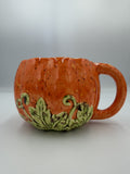Orange speckled ceramic pumpkin mug with sculpted green leaves and vines at the base