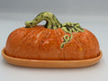 Orange speckled ceramic pumpkin butter dish with green stem and vine lid on matching tray