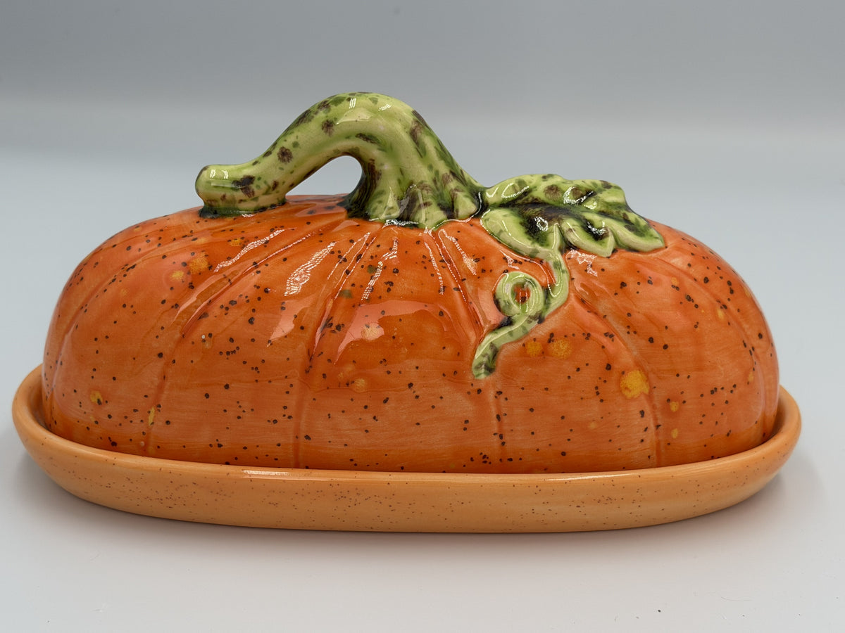 Orange speckled ceramic pumpkin butter dish with green stem and vine lid on matching tray