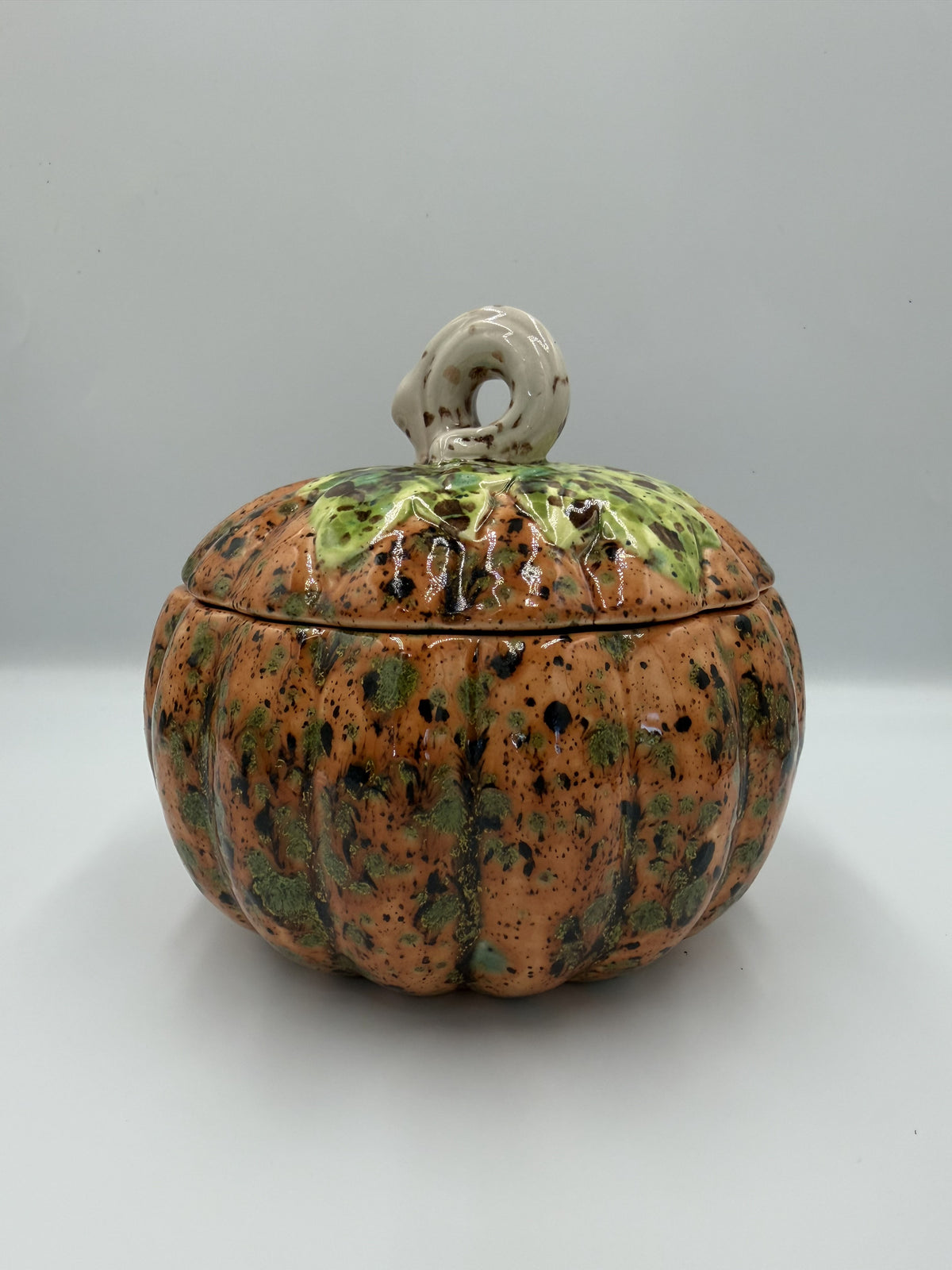 Caramel-orange speckled ceramic harvest pumpkin jar with green leafy lid and cream curly stem