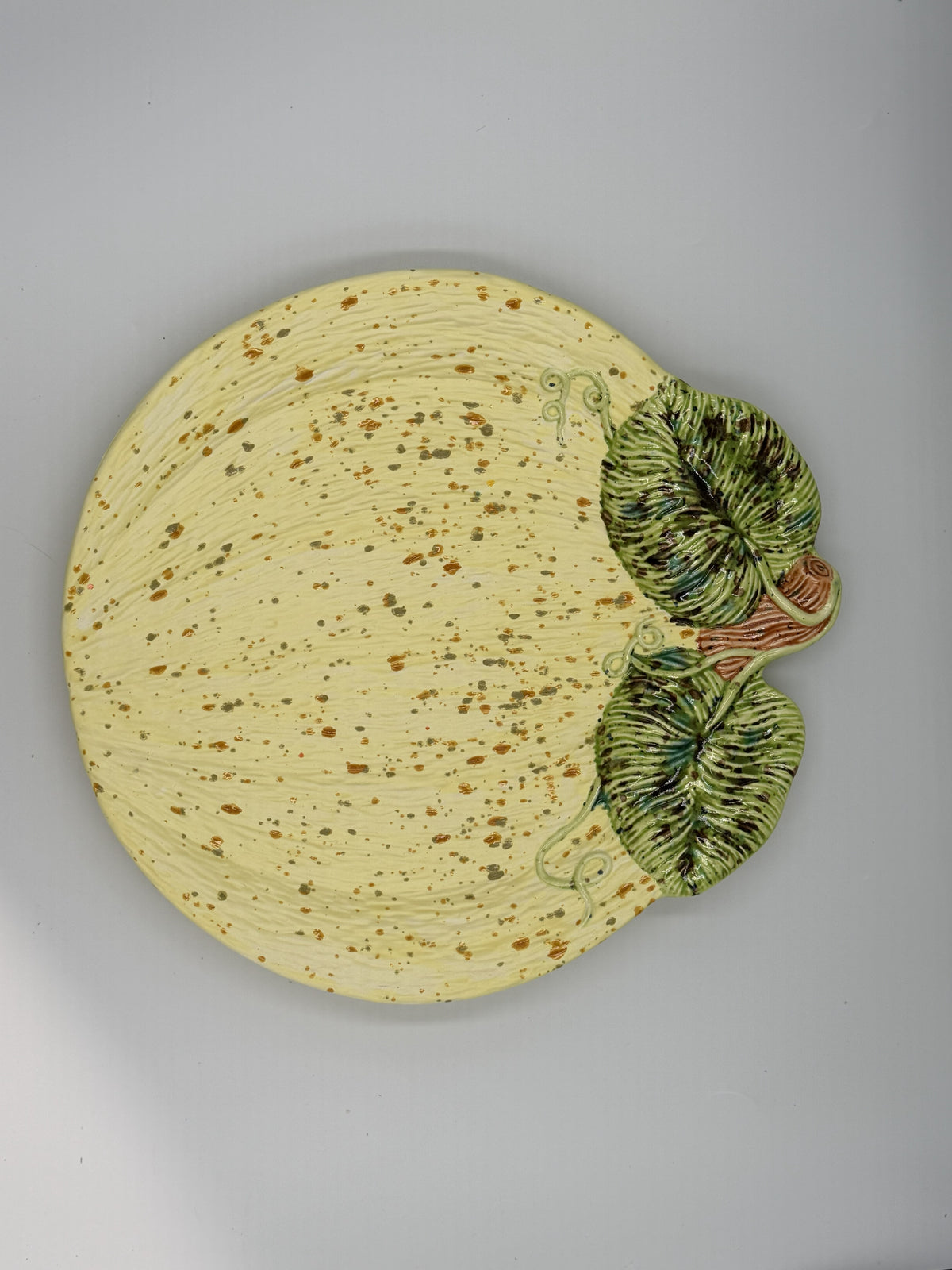 Cream speckled ceramic pumpkin-shaped plate with sculpted green leaves, stem, and vines