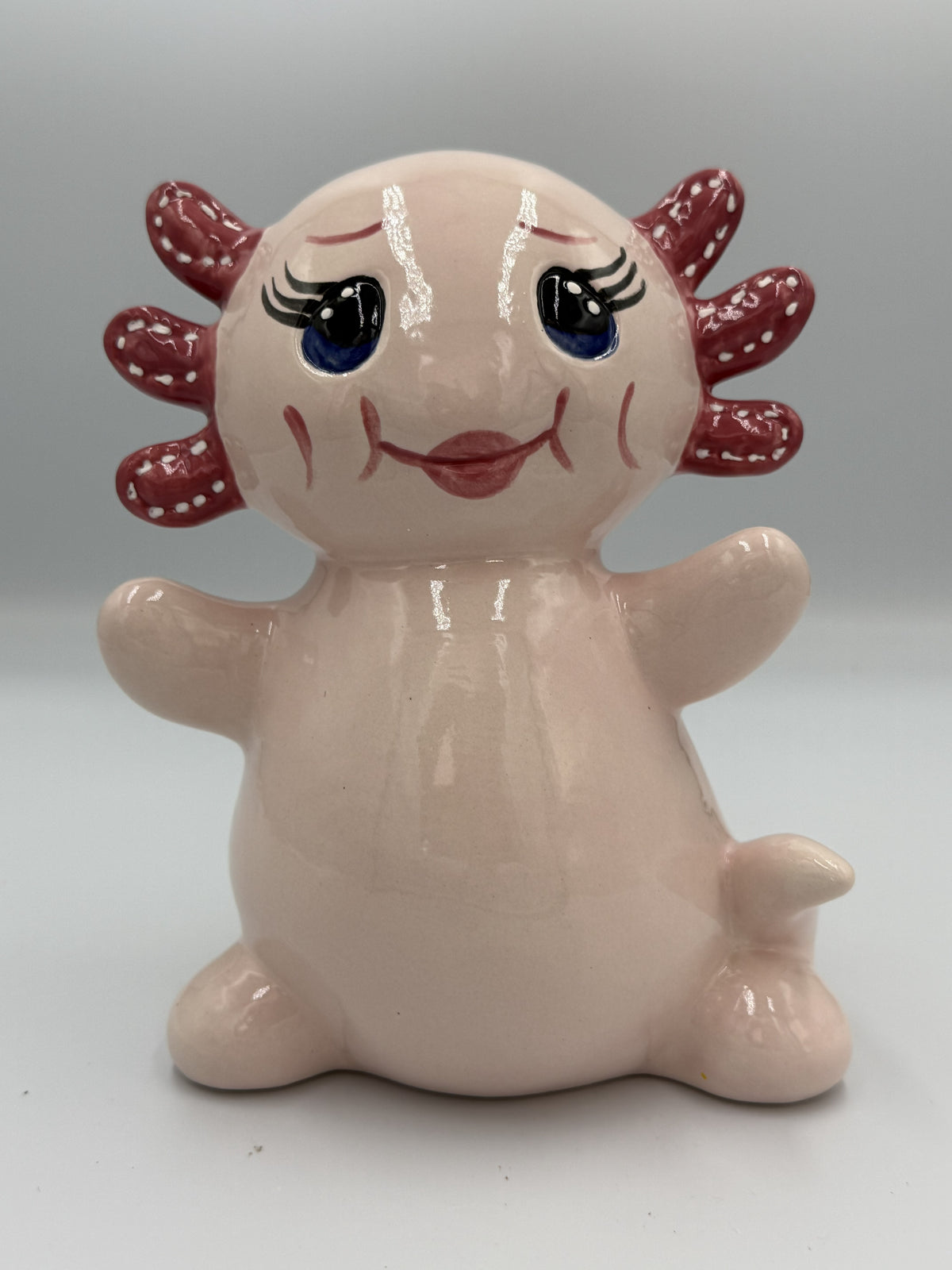 Large blush pink ceramic axolotl bank sitting upright with polka-dot gills and blue eyes