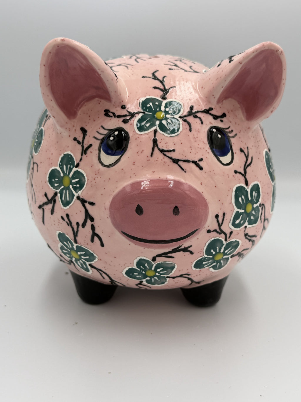 Front view of large pink speckled ceramic pig bank hand-painted with teal flowers and blue eyes