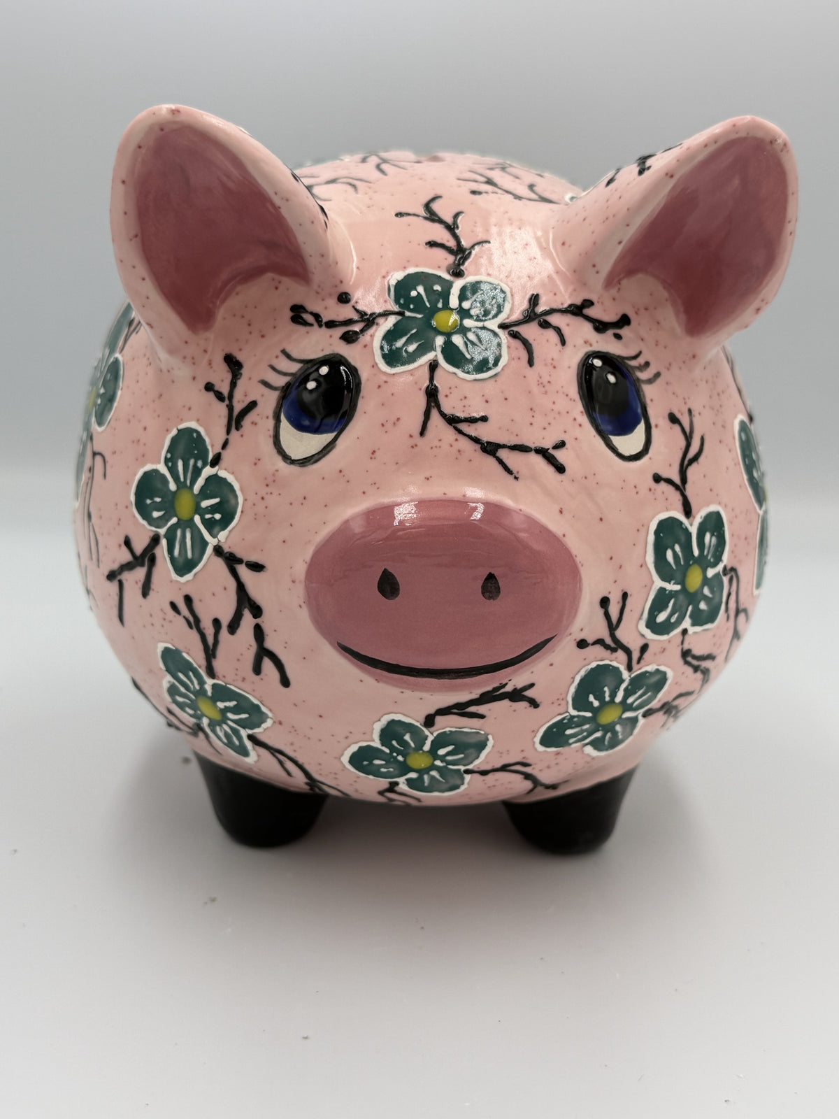 Front view of large pink speckled ceramic pig bank hand-painted with teal flowers and blue eyes