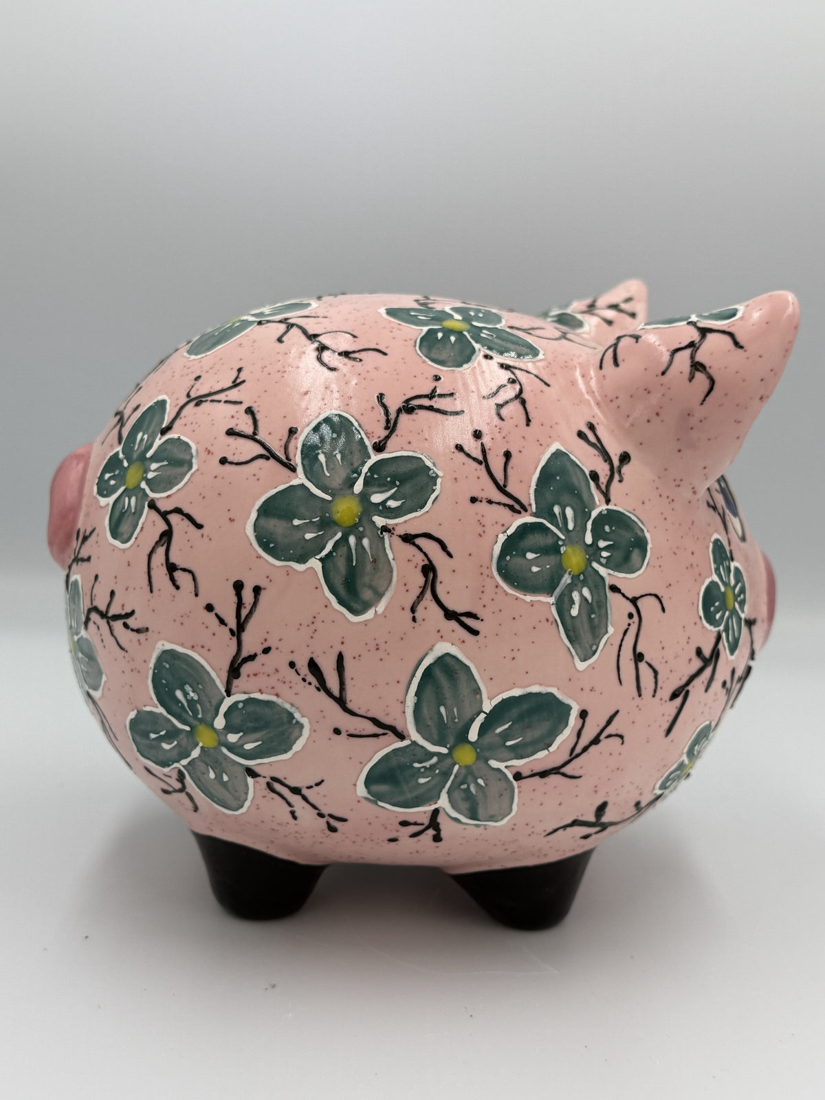 Side view of large pink ceramic pig bank covered in hand-painted teal blossoms and black branches