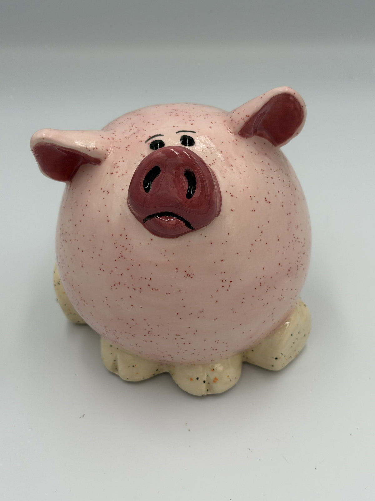 Round light pink speckled ceramic pig bank with rosy snout and ears and cream hooves