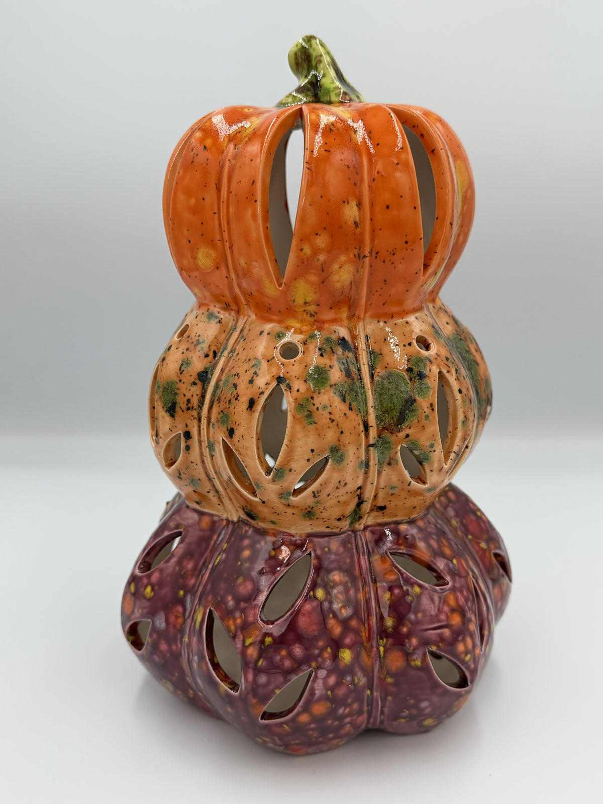 Stacked ceramic pumpkin lantern in orange, peach, and plum with leaf-shaped cutouts