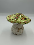 Ceramic mushroom with glossy green cap speckled in orange and brown, and ribbed cream stem