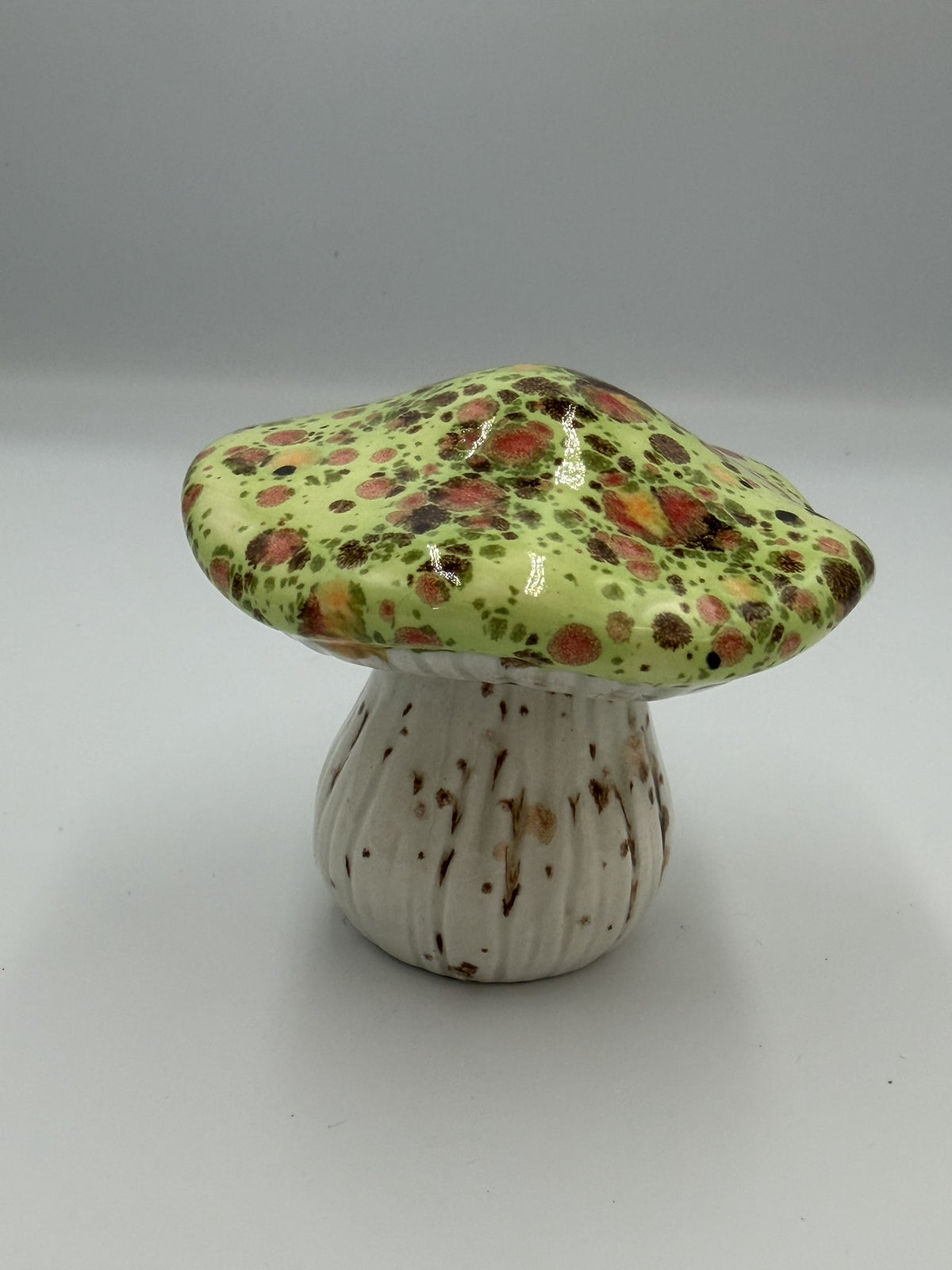Ceramic mushroom with glossy green cap speckled in orange and brown, and ribbed cream stem
