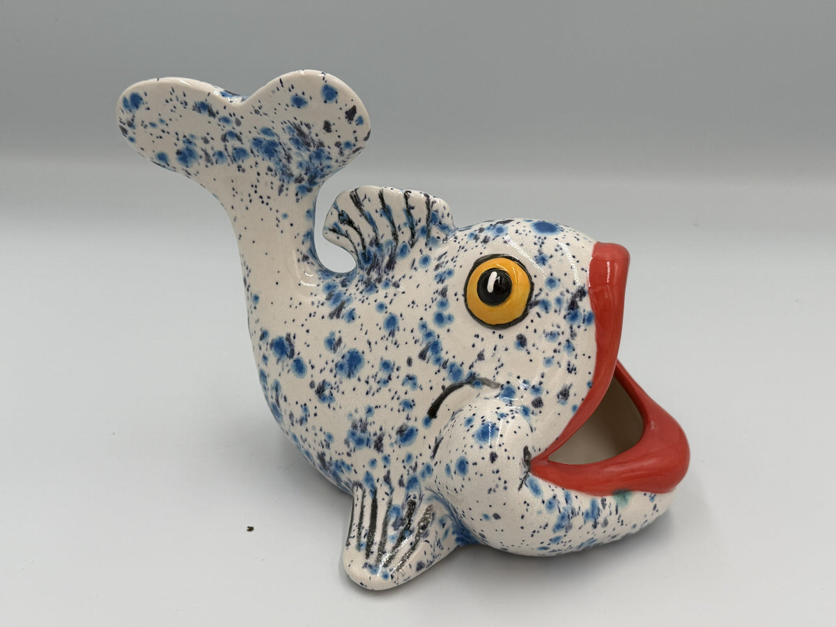 White ceramic fish scrubby holder with blue speckles, amber eye, and wide red open mouth