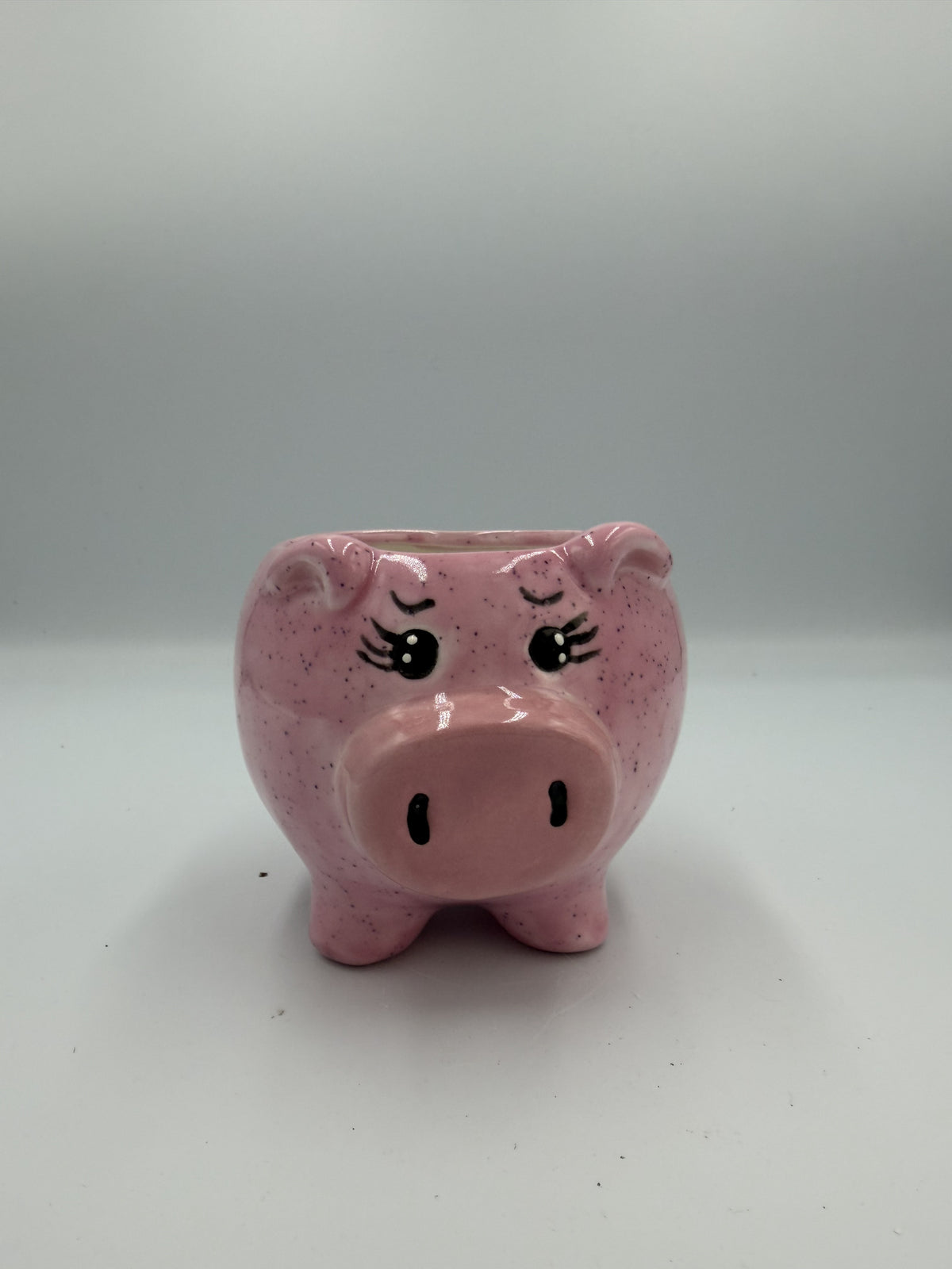 Side view of a glossy pink pig-shaped mug showing its handle, feet, and tail