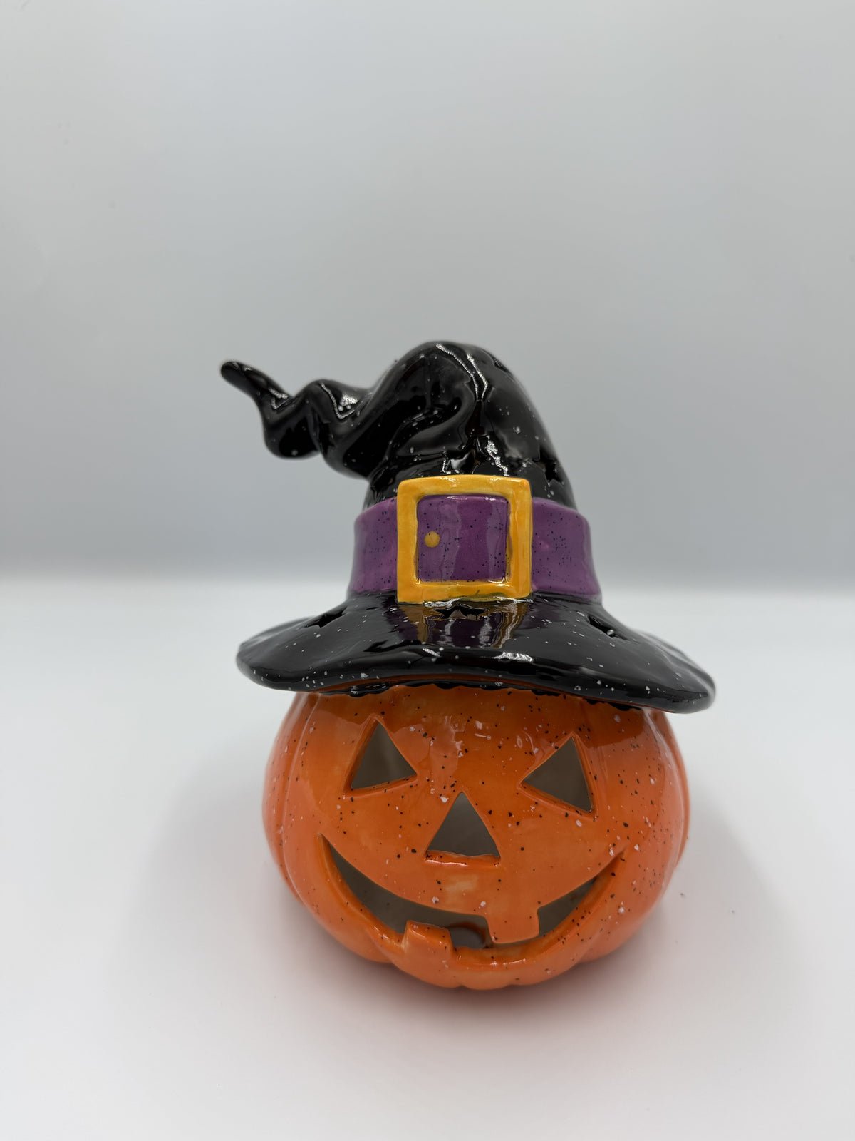Orange ceramic jack-o'-lantern wearing a black witch hat with purple band and gold buckle
