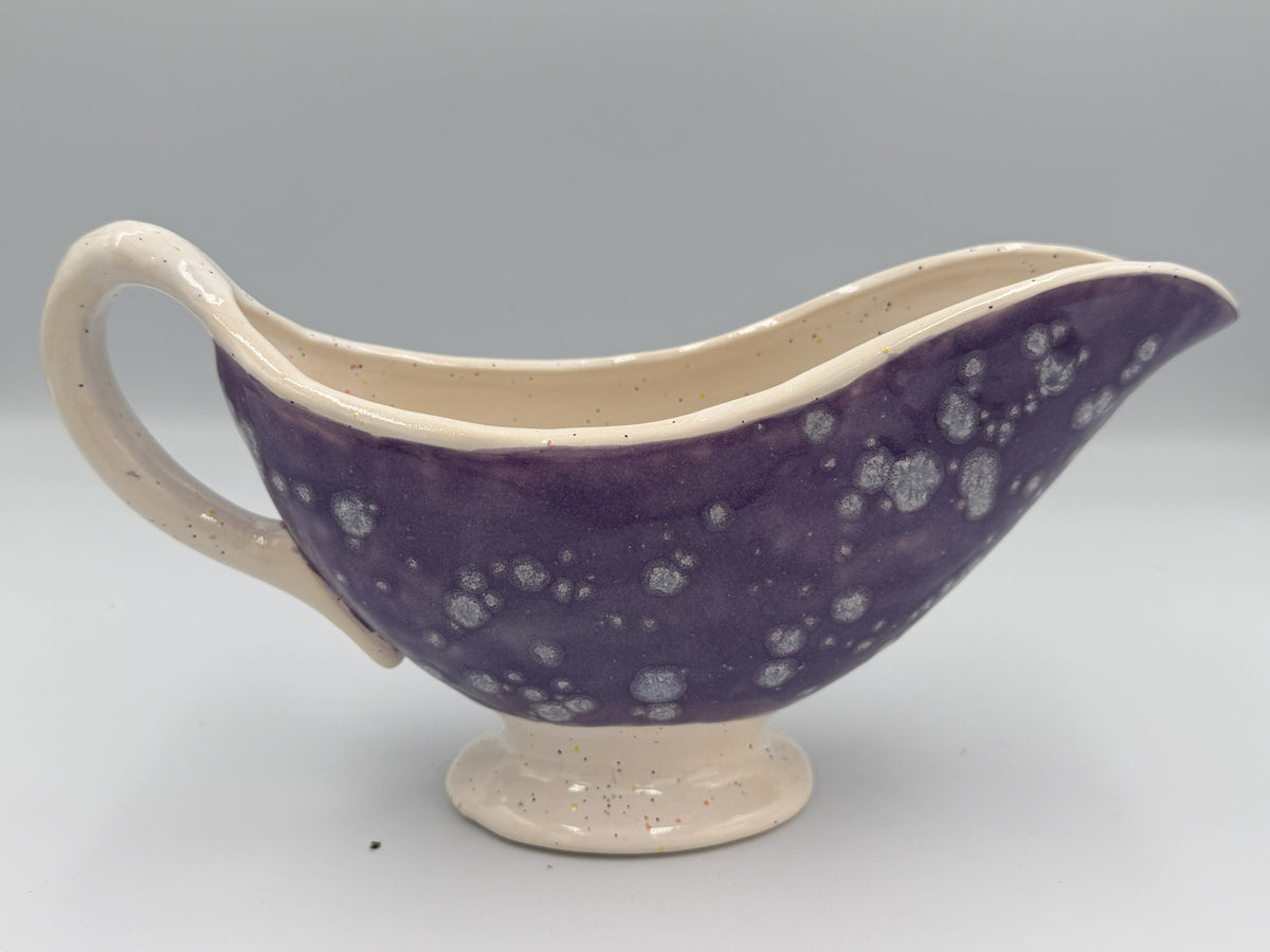 Purple speckled ceramic gravy boat with cream rim, handle, and foot