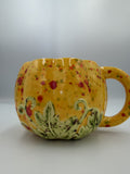 Yellow ceramic pumpkin mug with red, orange, and green speckles and sculpted green leaves at the base