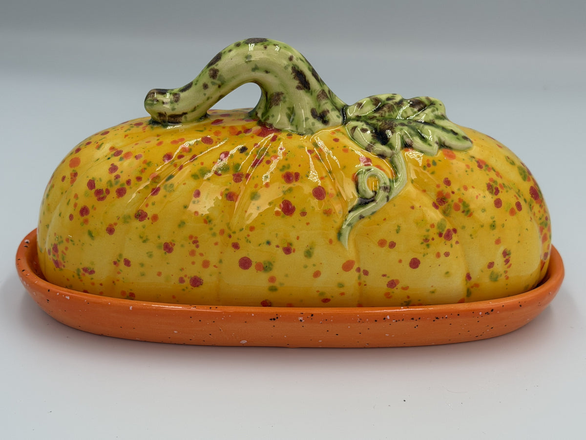 Yellow speckled ceramic pumpkin butter dish with green stem and vine lid on orange tray
