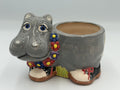 Grey ceramic hippo planter with blue eyes, flower garland, and black polka-dot shoes