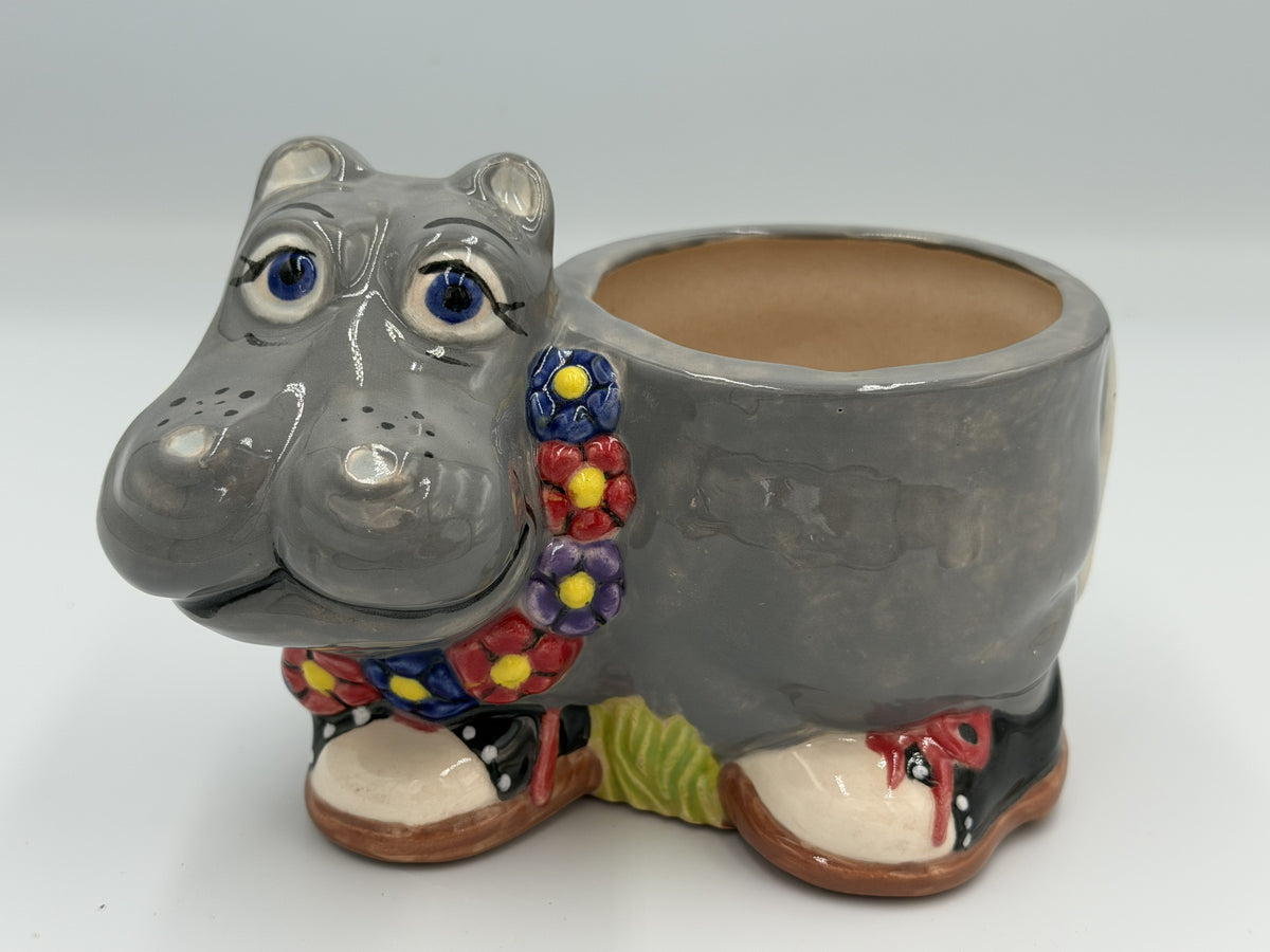 Grey ceramic hippo planter with blue eyes, flower garland, and black polka-dot shoes
