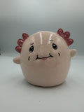 Round blush pink ceramic axolotl bank with frilly pink gills, blue eyes, and a smile
