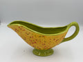 Yellow speckled ceramic gravy boat with lime green rim, handle, and foot