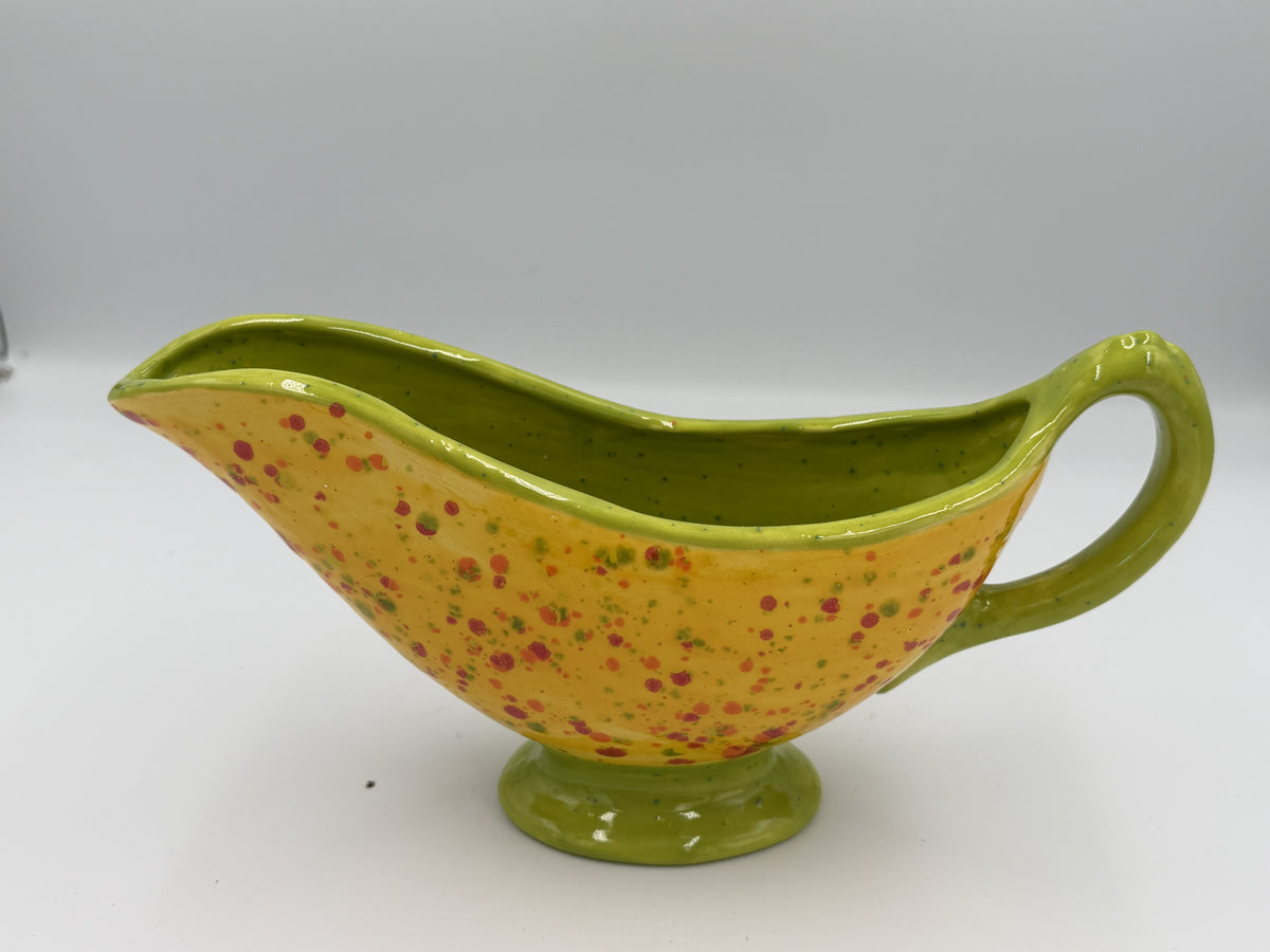 Yellow speckled ceramic gravy boat with lime green rim, handle, and foot